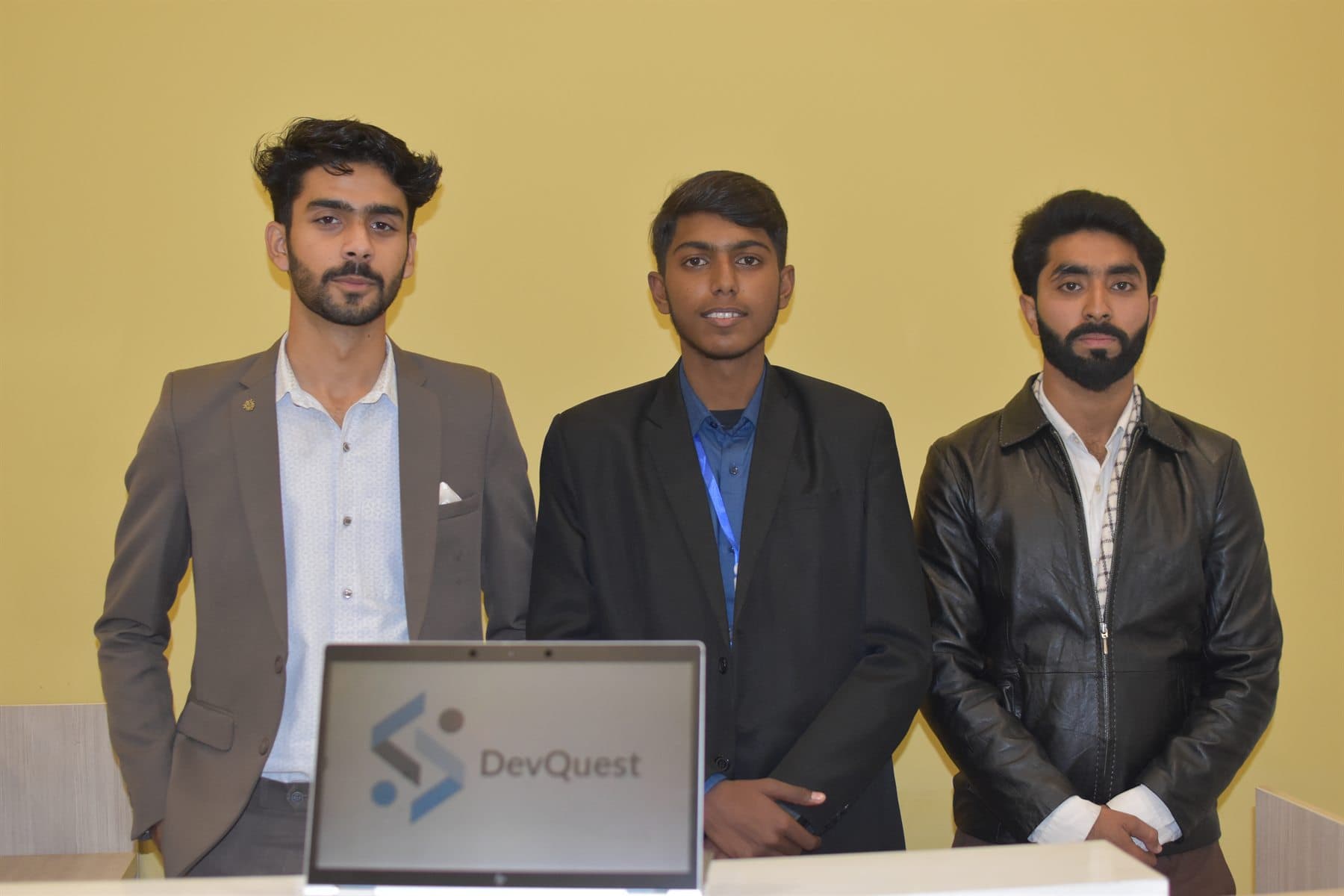 DevQuest team members standing behind a laptop displaying the DevQuest logo